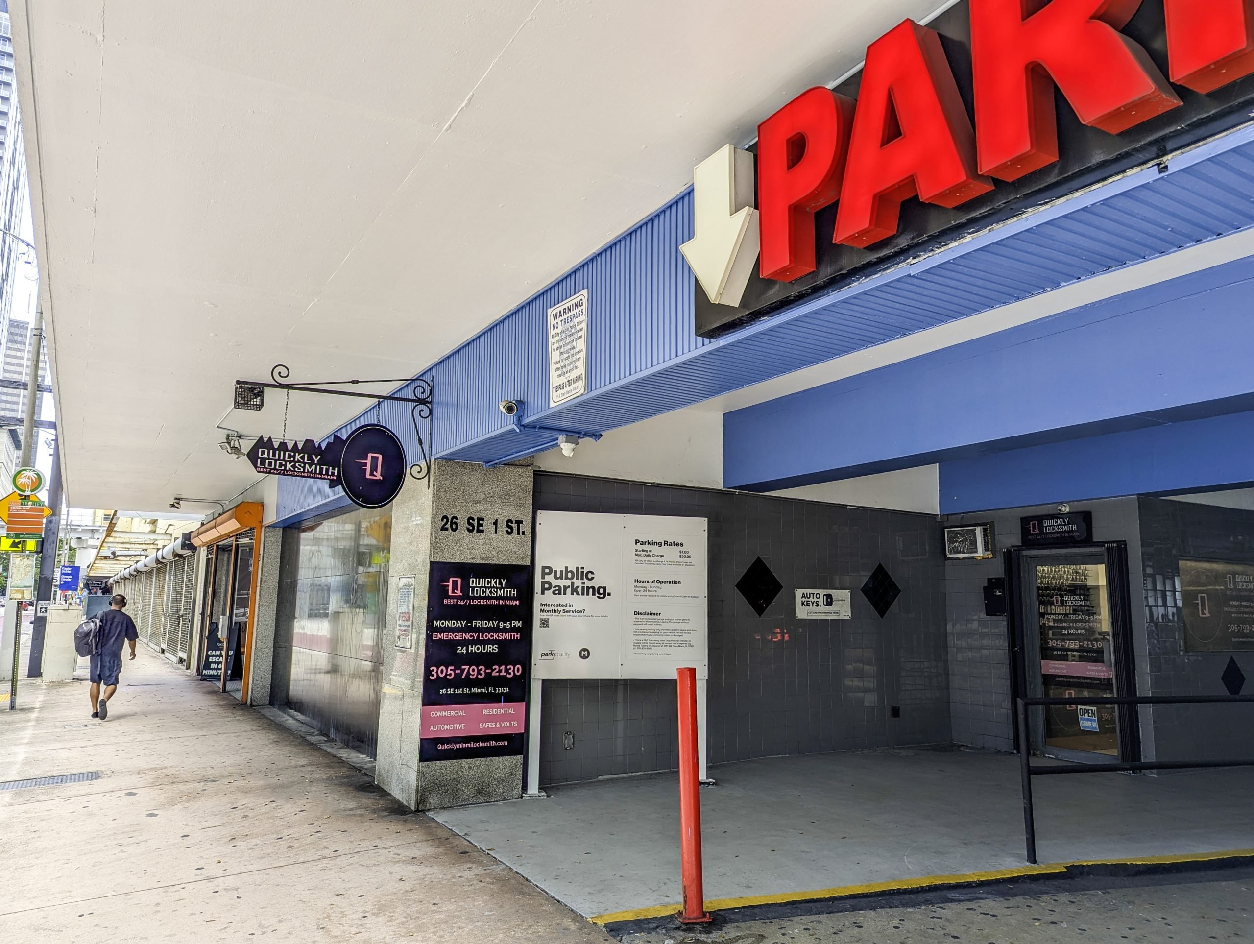 Parking garage entrance with red sign and Quickly Locksmith Miami Downtown shop tucked in the corner with directional signage.
